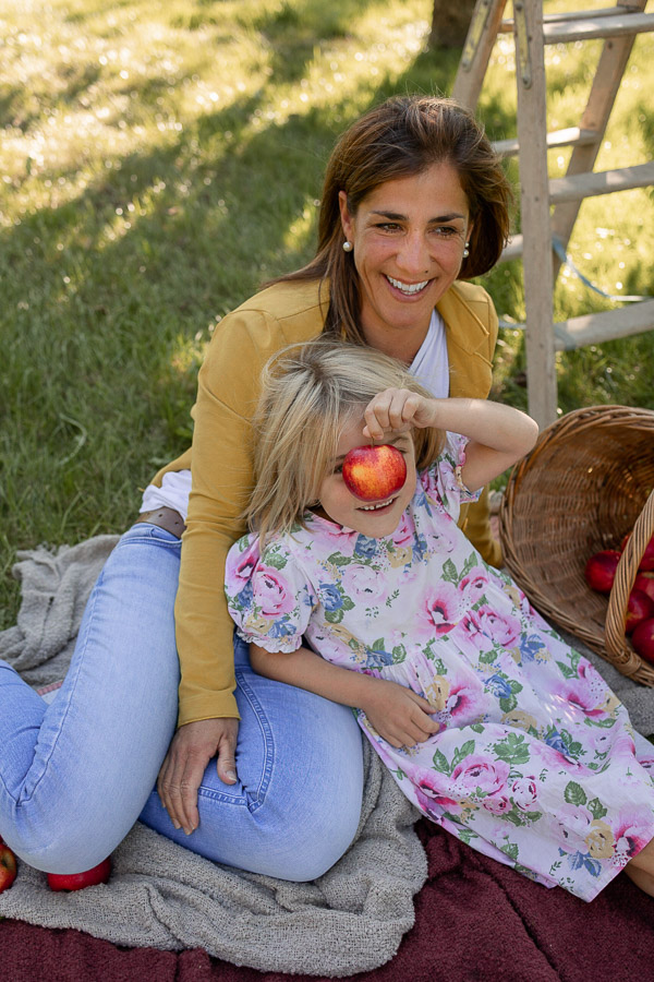 Familienfotografie. Mutter und Tochter bei einem herbstlichen Fotoshooting. Tochter hat Apfel vorm Gesicht.